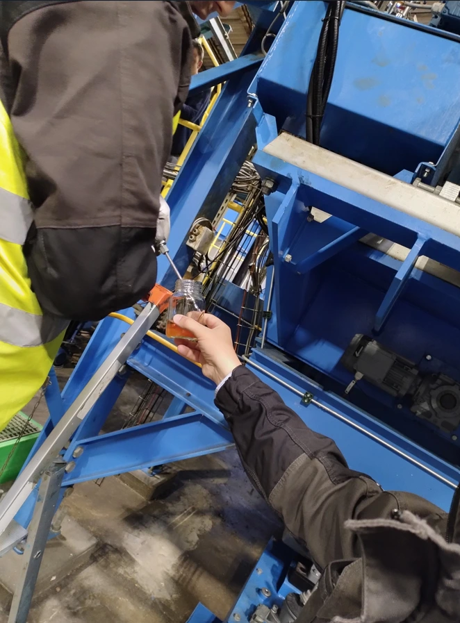 Technicien réalisant un prélèvement d'huile hydraulique sur une installation industrielle dans le cadre d'une analyse de maintenance prédictive.